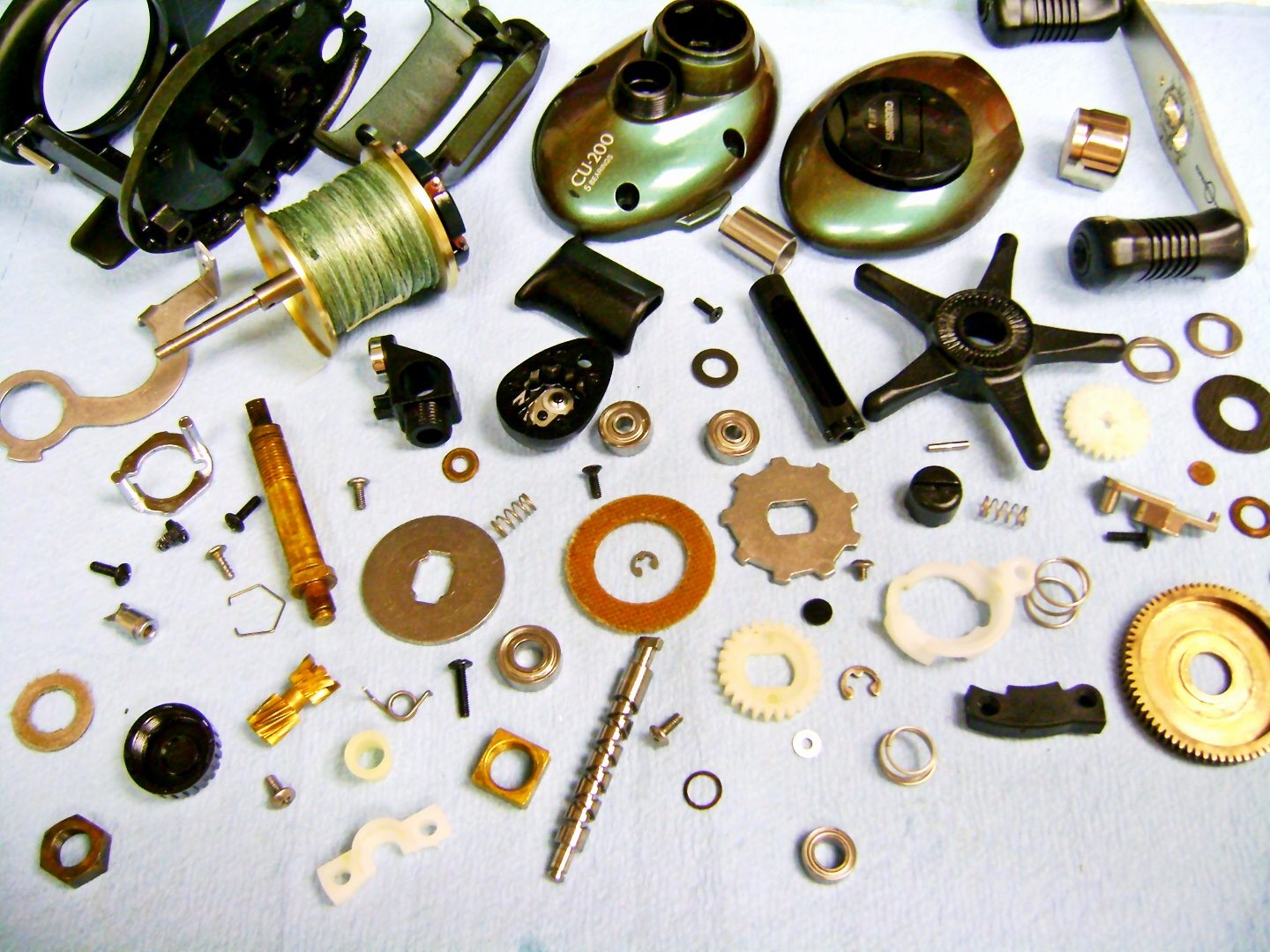 A baitcasting reel fully broken down into its parts on the shop bench
